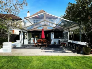 Marquee outside over wooden tables with red parasol in sunny garden.