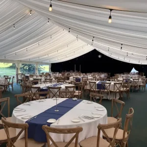 Interior of large luxry wedding marquee with navy table runner draped over circle tables
